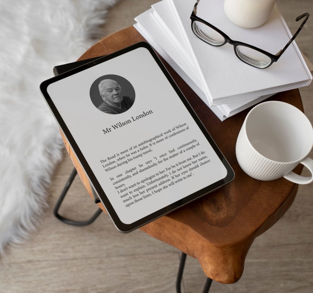 An e-reader sits on a little wooden designer coffe table with a mug and glasses and books beside it. There is a sheepskin rug on the floor.