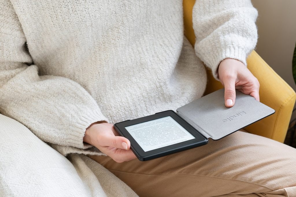A man with a cosy-looking white woollen sweater sits reading an e-reader on his lap.