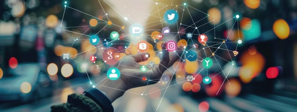 A hand holding what looks like a network of social media connections - little icons spread out in different colours and joined by thin white threads of connection.